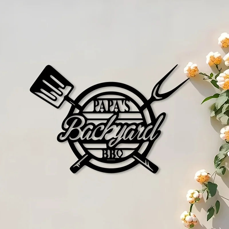 Black wall decor featuring a silhouette of a fork and knife surrounding the text Papa's Backyard BBQ