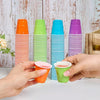 A hand holds a stack of colorful disposable plastic shot cups in various shades of orange, green, blue, and purple.