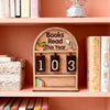 Un support de suivi de livres en bois avec des emplacements étiquetés 1, 0 et 3 sur une étagère rose.
