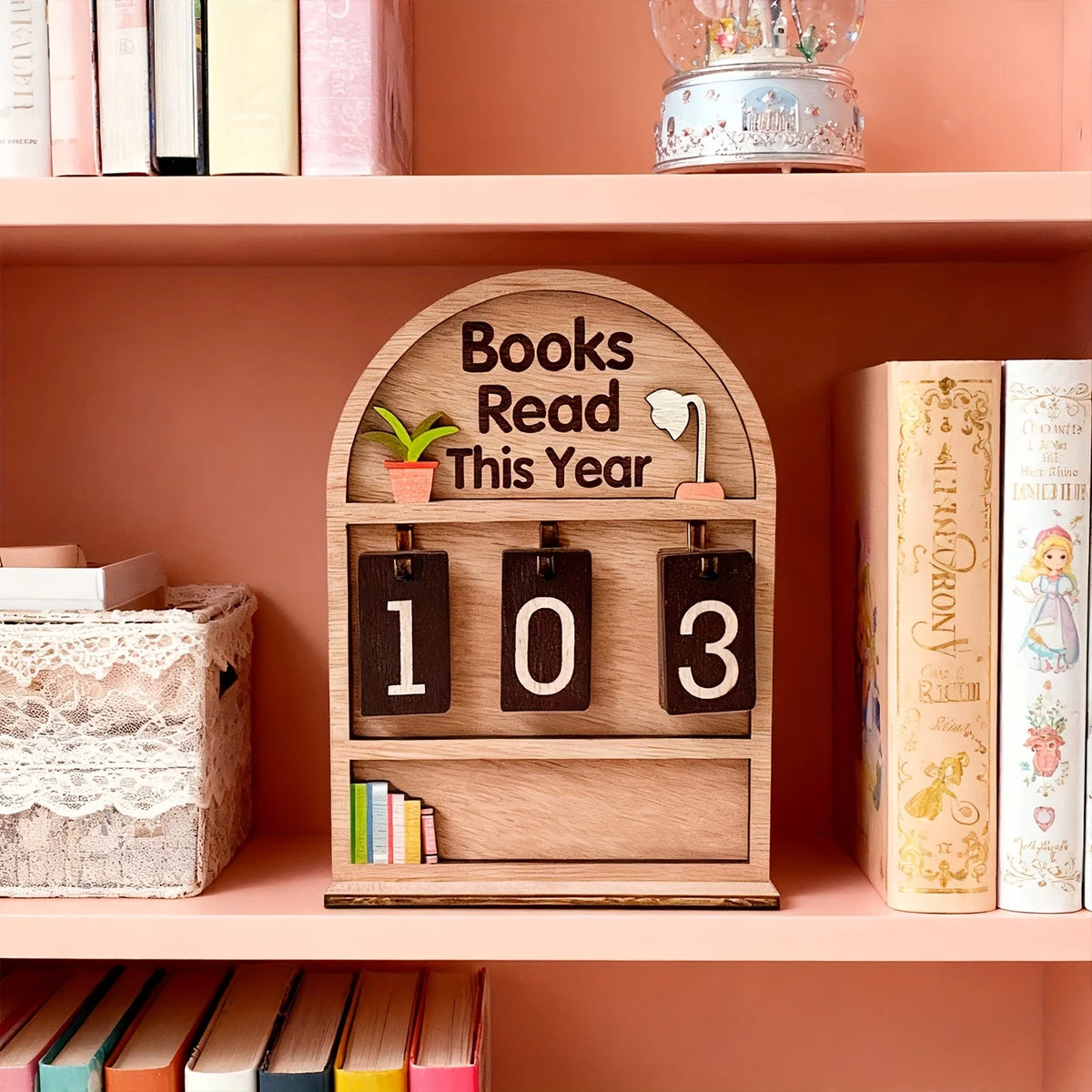 Un support de suivi de livres en bois avec des emplacements étiquetés 1, 0 et 3 sur une étagère rose.