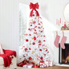 A white artificial Christmas tree decorated with red ornaments and bows, standing next to a fireplace.