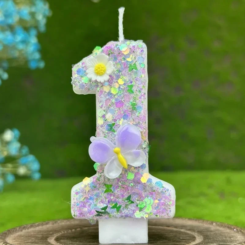A tall candle shaped like the number one decorated with purple and green glitter, a butterfly, and a white flower.