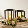 A rustic wooden candle holder lantern with a rectangular frame and glowing candle placed on a beige fabric.