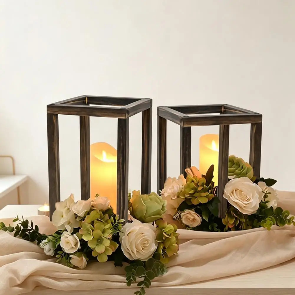 A rustic wooden candle holder lantern with a rectangular frame and glowing candle placed on a beige fabric.