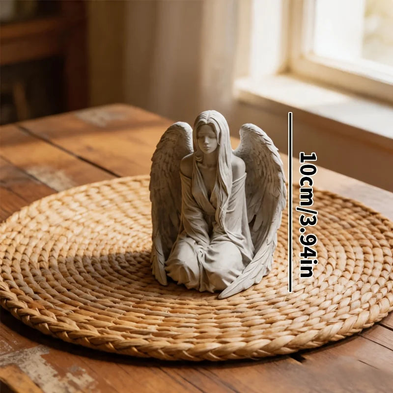 Estatuilla decorativa de ángel gris claro con alas, colocada sobre una estera tejida en una superficie de madera.