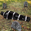 A black body wrapped in silver stripes lies on grass with RIP grave markers nearby.