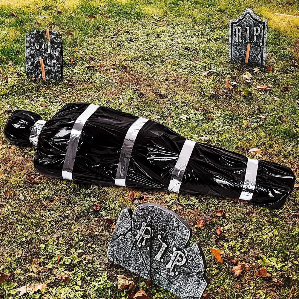 A black body wrapped in silver stripes lies on grass with RIP grave markers nearby.