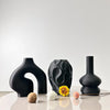 A set of three matte black geometric vases displayed on a white surface.