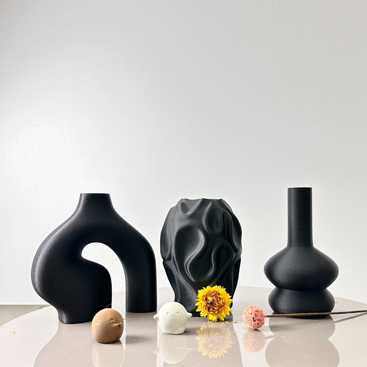 A set of three matte black geometric vases displayed on a white surface.