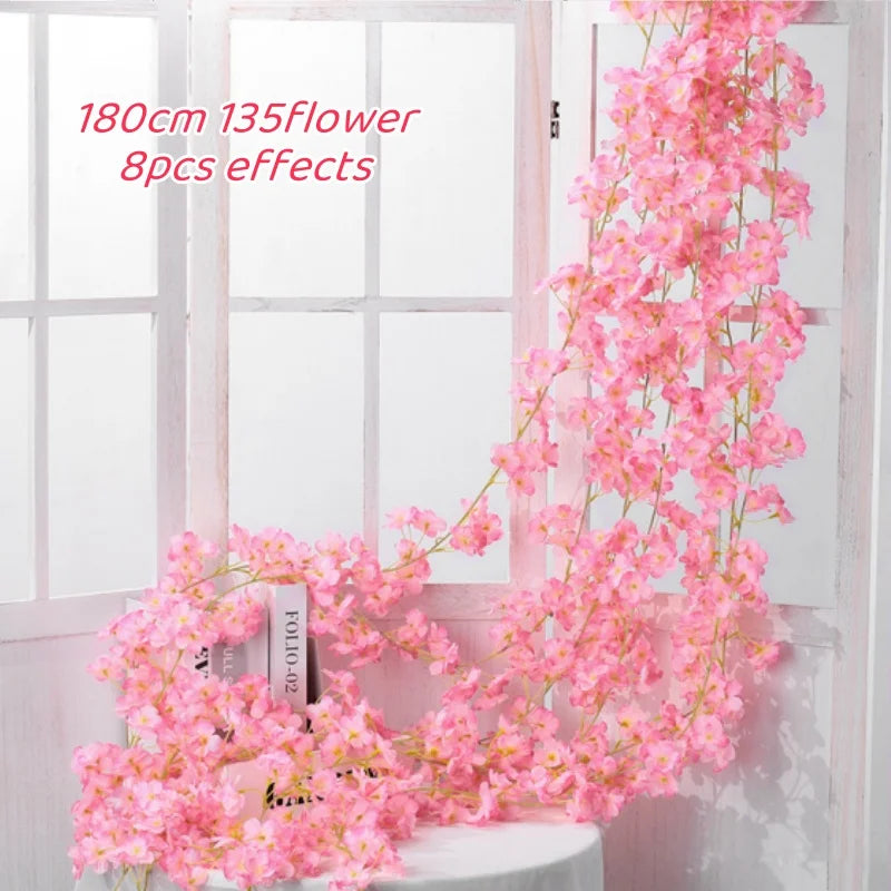 A long pink sakura flower garland is displayed against a white window frame.