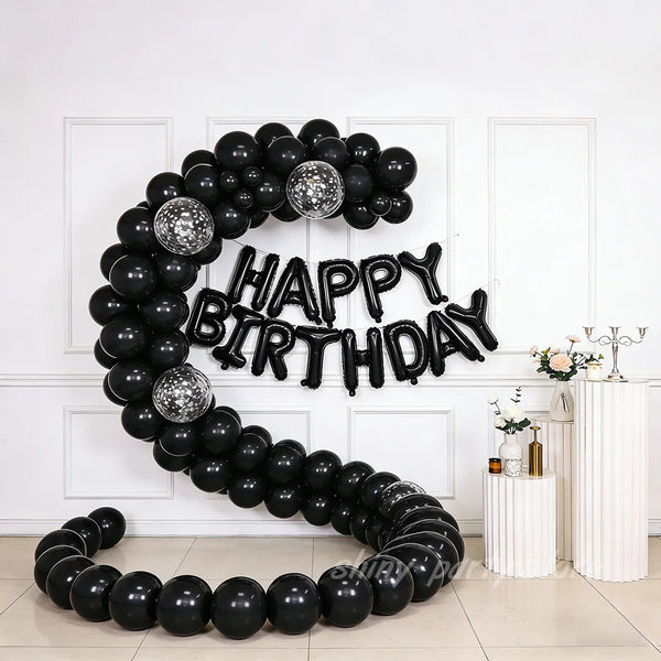 A black latex balloon garland shaped like a horseshoe for a birthday celebration against a white wall.