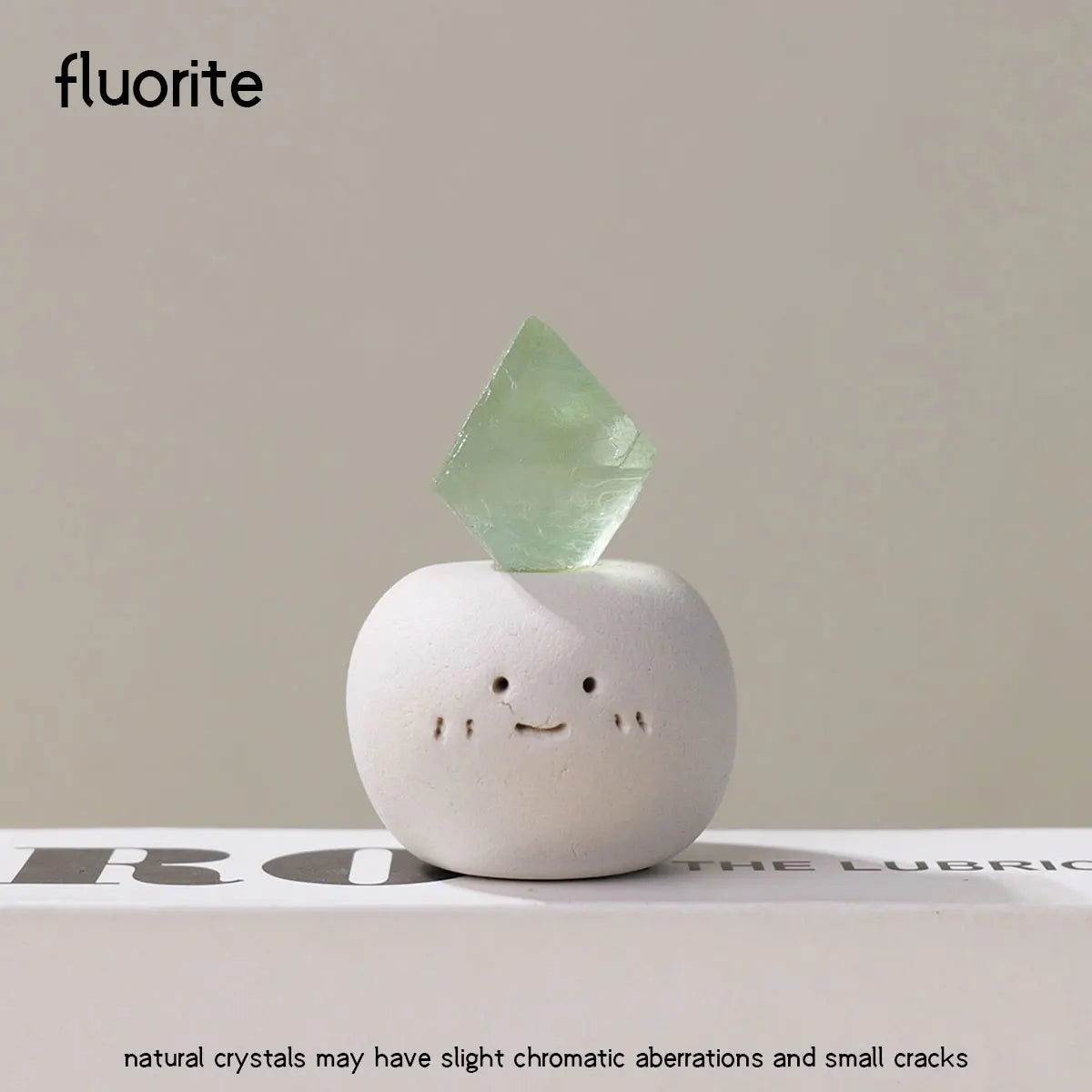 A smooth, light green fluorite crystal sits atop a white, bean-shaped decorative stone.