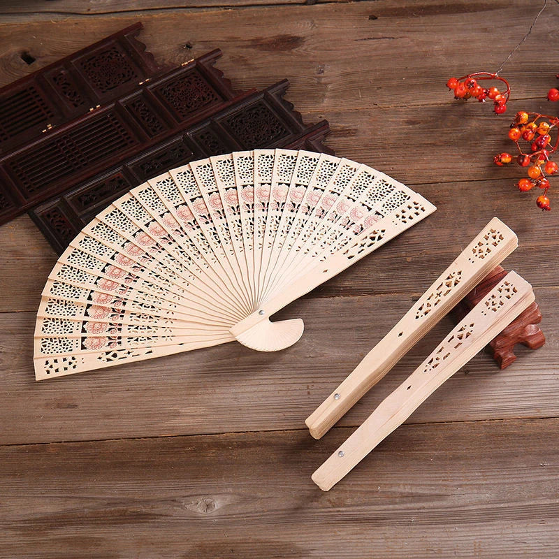 Hand carved bamboo folding fan with intricate cutouts resting on a wooden surface.
