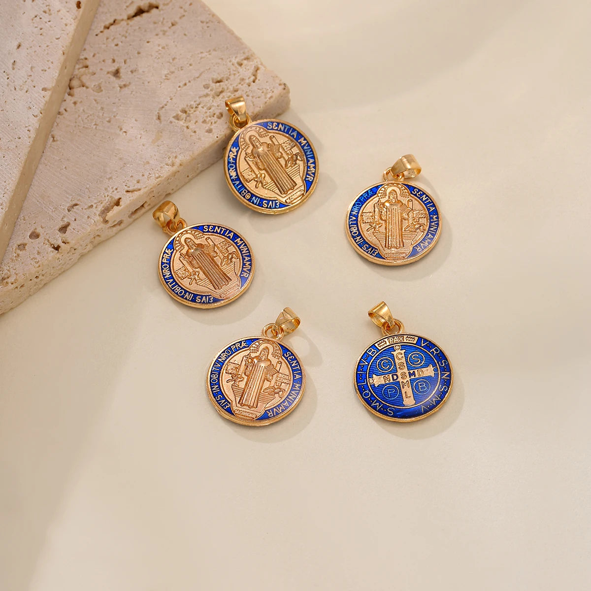 A set of twelve gold-toned double-sided St. Benedict medals featuring religious imagery and text on a white background.