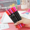 A hand holds a set of dual-ended watercolor art markers in various bright colors, resting on a white tray.