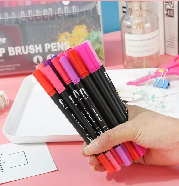 A hand holds a set of dual-ended watercolor art markers in various bright colors, resting on a white tray.