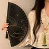 A woman holds a black folding hand fan with a leopard print design and a black handle.