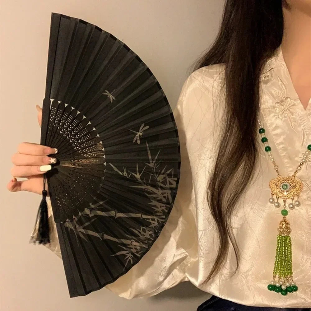 A woman holds a black folding hand fan with a leopard print design and a black handle.