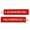 Red woven tag with white text that reads Kiss Me Before Flight and a metal keyring.