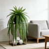 Artificial Persian fern hanging vine in a black pot displayed on a gold-framed stand next to a sofa.