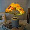 A bright yellow sunflower LED night light in a cylindrical pot sits on a book.