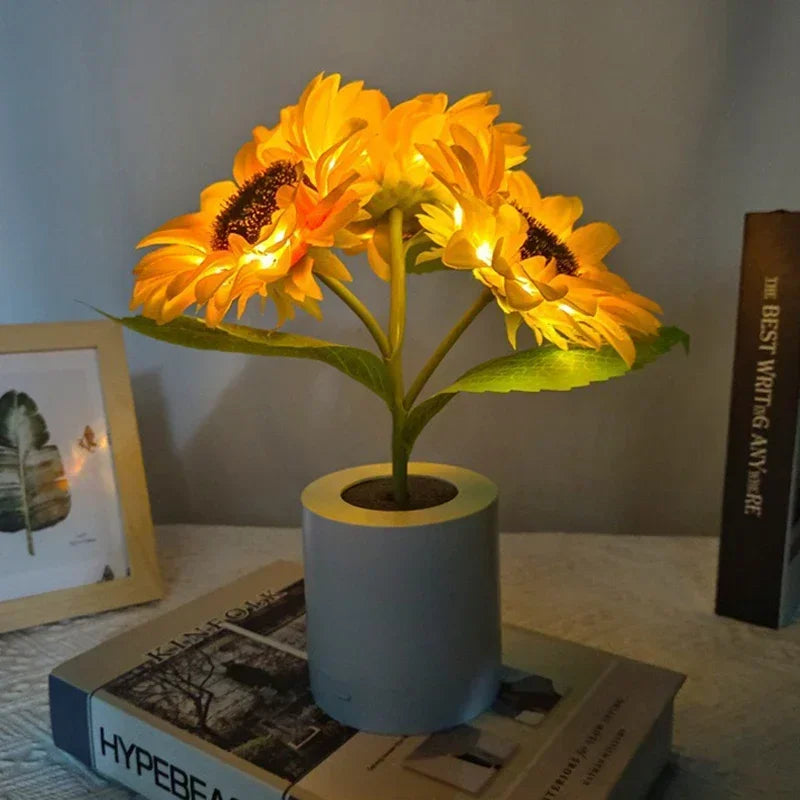 A bright yellow sunflower LED night light in a cylindrical pot sits on a book.