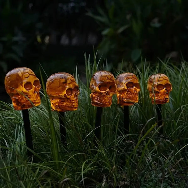 A row of orange skull solar pathway lights emerging from green grass.