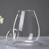 A clear glass vase with a rounded shape sits on a gray surface, featuring small decorative elements.