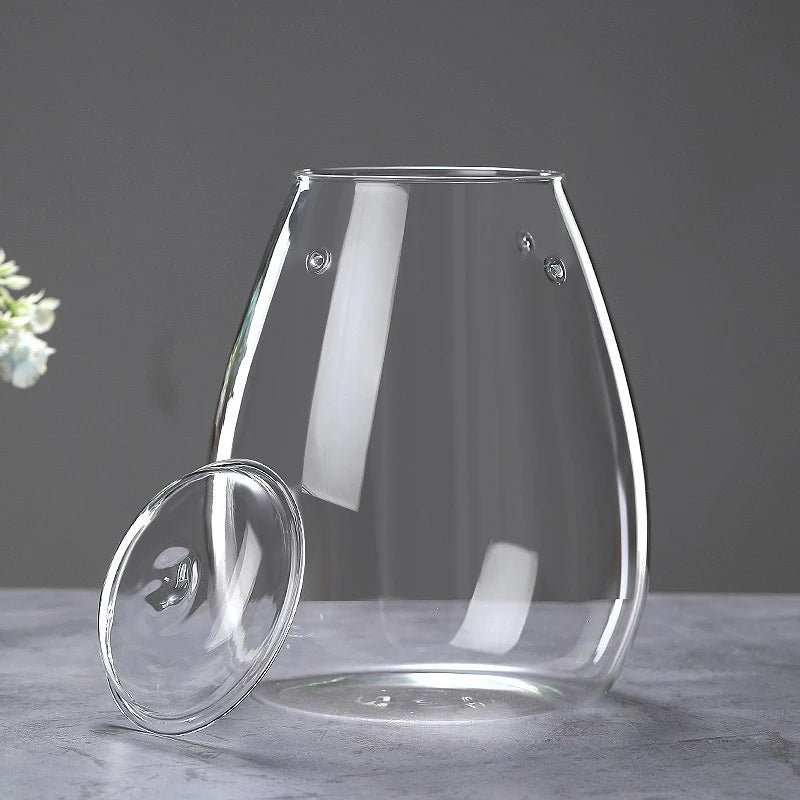 A clear glass vase with a rounded shape sits on a gray surface, featuring small decorative elements.
