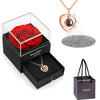 Un coffret noir contenant une rose rouge conservée, un collier cœur doré et un charm argenté.