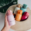 A hand holds a pink vacuum insulated coffee mug next to several colored stainless steel vacuum insulated coffee mugs on a str