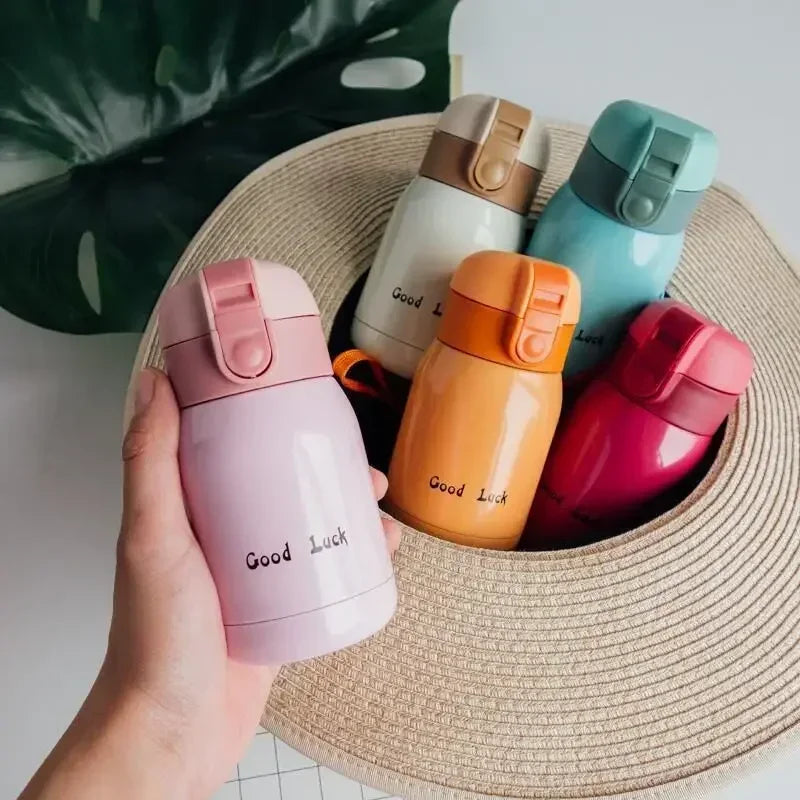 A hand holds a pink vacuum insulated coffee mug next to several colored stainless steel vacuum insulated coffee mugs on a str