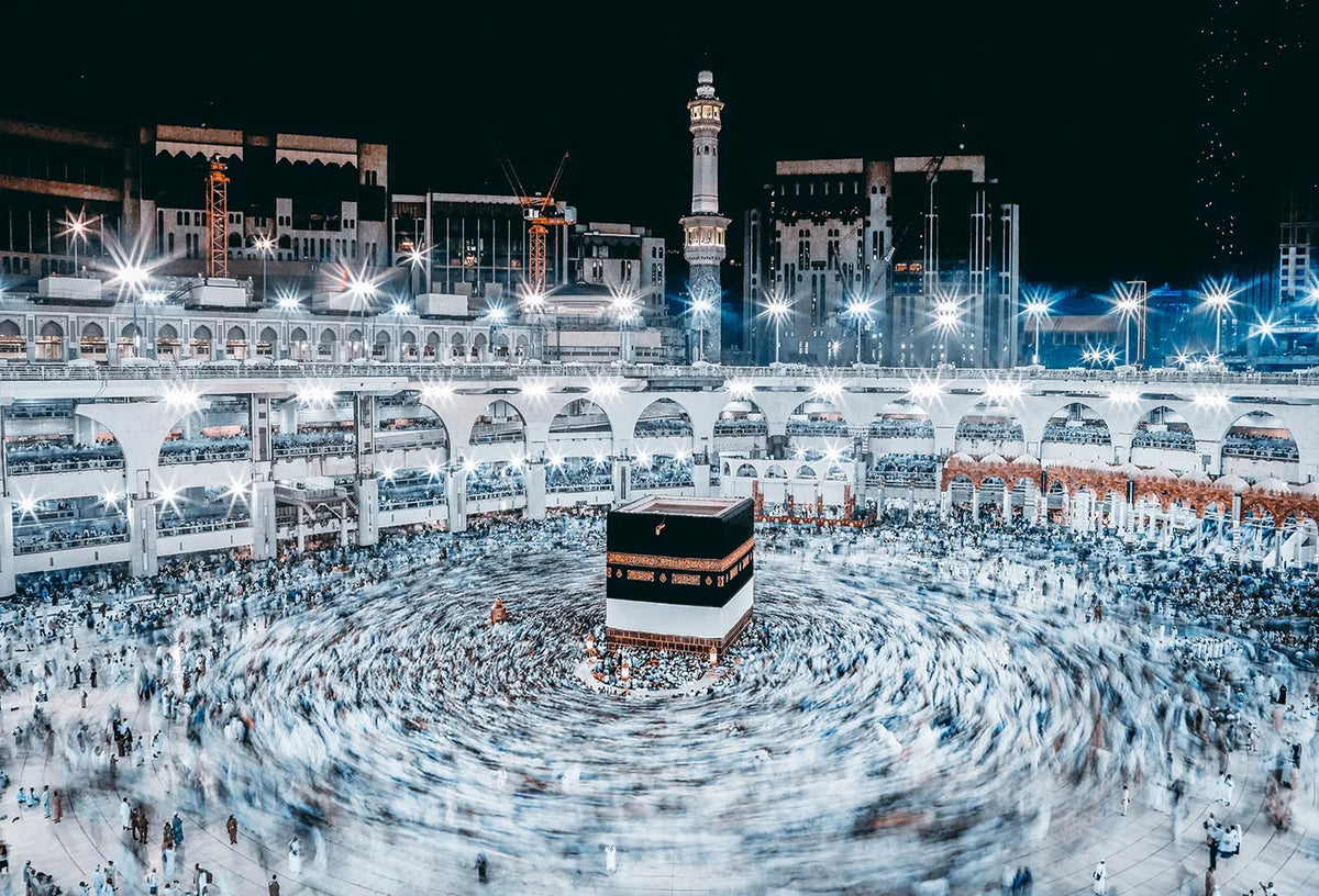 A wide-angle night shot of a large crowd gathered in a circle, with an illuminated mosque and cityscape in the background.