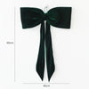 A dark emerald green velvet bow with long tails, used as a Christmas tree ornament.