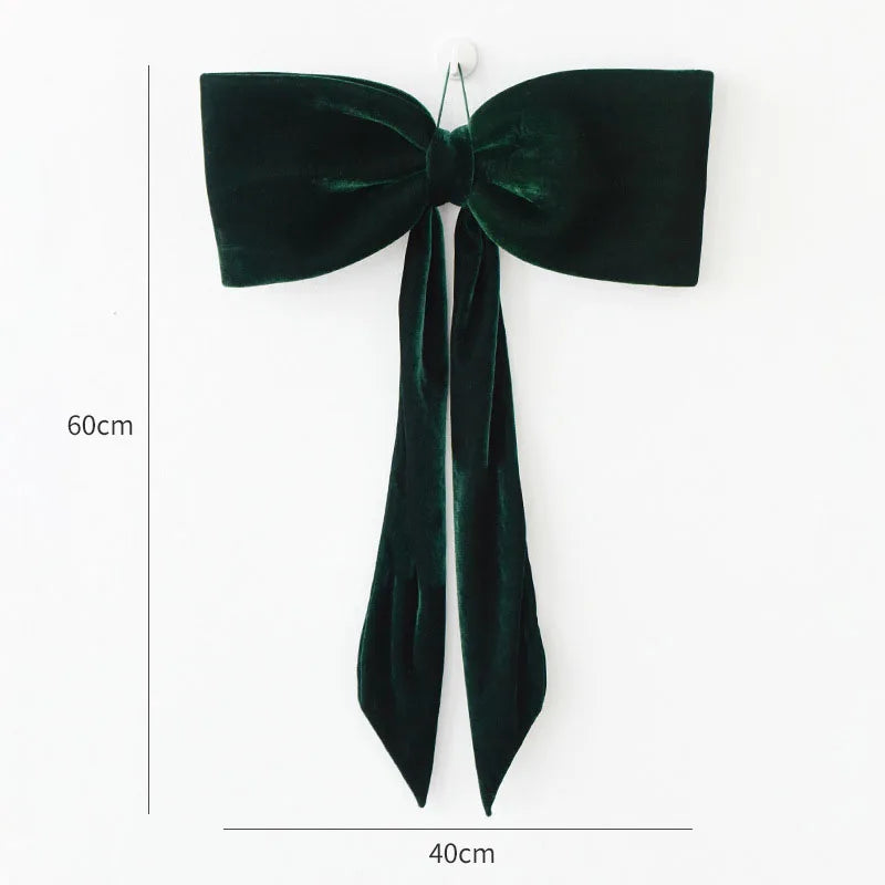 A dark emerald green velvet bow with long tails, used as a Christmas tree ornament.