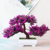 Un arbre bonsaï artificiel réaliste avec un feuillage magenta vibrant, présenté dans un pot blanc.