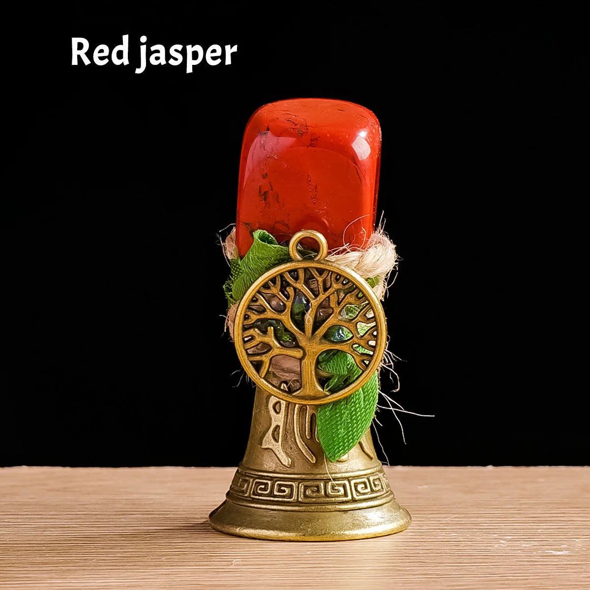 A red jasper tree of life chime with a golden bell and green leaves resting on a wooden surface.