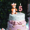 A two-tiered birthday cake decorated with pink and mint green frosting, featuring a teddy bear topper and a large pink number