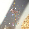 A hanging crystal dreamcatcher sun catcher featuring a pink moon and colorful prism drops.