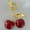Gold-toned pendant keychain featuring two shiny red resin cherries with glitter accents.