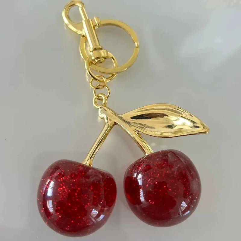 Gold-toned pendant keychain featuring two shiny red resin cherries with glitter accents.