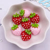 Pink and red strawberry resin flatback charms arranged in a white dish for DIY crafts