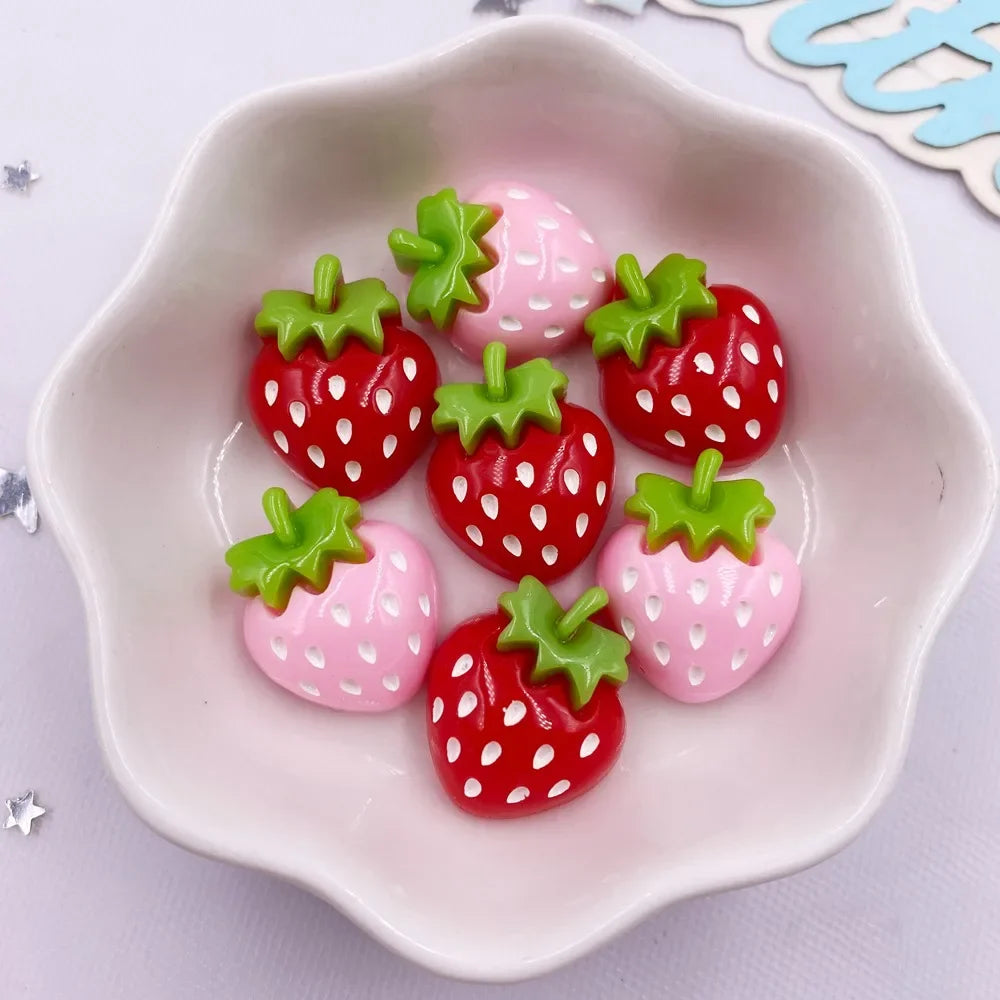 Pink and red strawberry resin flatback charms arranged in a white dish for DIY crafts