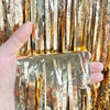 A hand holds metallic gold tinsel foil fringe curtain backdrop for parties