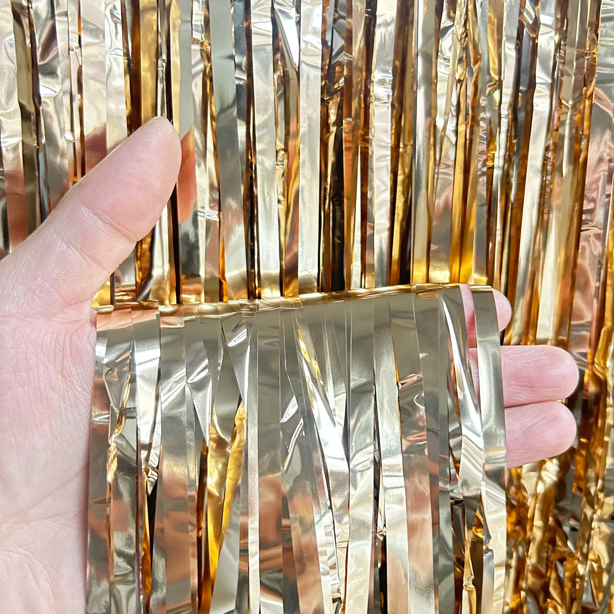 A hand holds metallic gold tinsel foil fringe curtain backdrop for parties