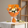 A bouquet of handmade crochet rose flowers in orange paper wrapping displayed on a white table.