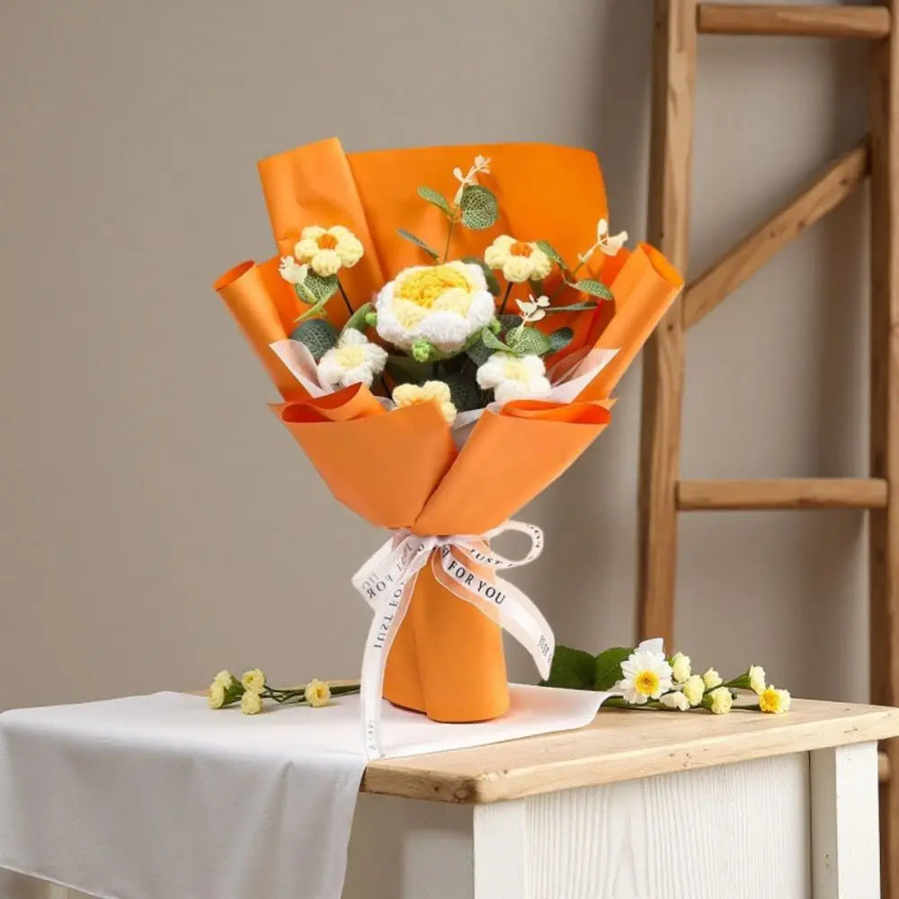 A bouquet of handmade crochet rose flowers in orange paper wrapping displayed on a white table.