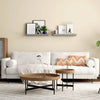 A living room wall decorated with two floating wood shelves displaying framed art and greenery.