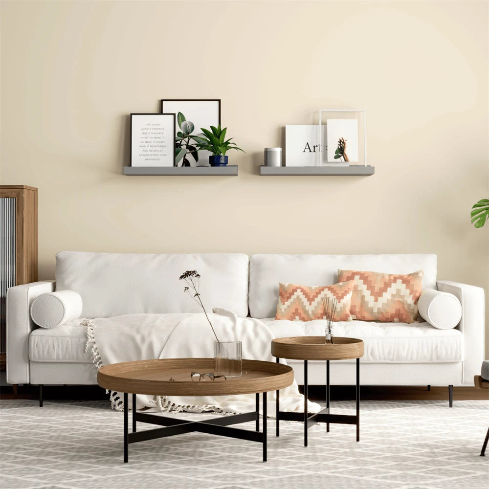 A living room wall decorated with two floating wood shelves displaying framed art and greenery.