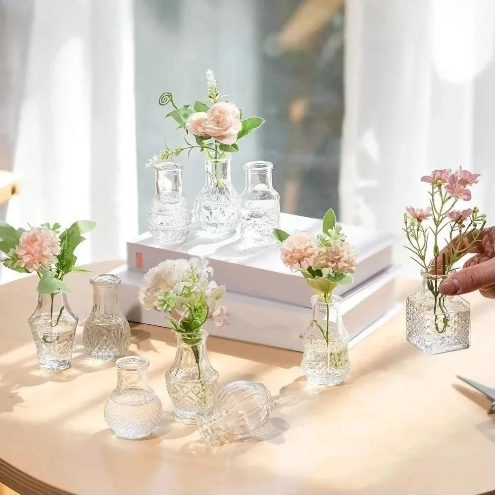 A collection of diamond faceted glass bud vases holding pink and green floral arrangements on a light wooden surface.